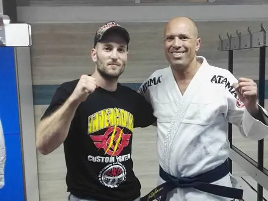 Alejandro Tebar y otro deportista, con el puño en alto, en un vestuario. Uno de los dos lleva kimono de BJJ.